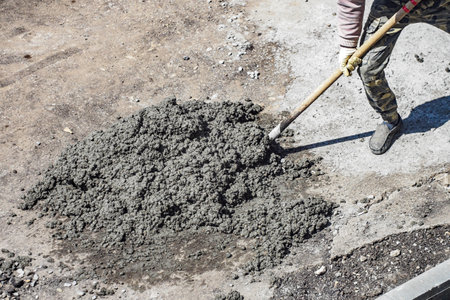 Road surface repair. Handyman with shovel scatters cement along road from pile. Planned elimination of bumps and holes on road.の写真素材