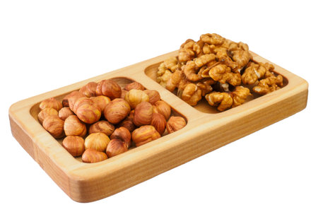 Wooden rack with assorted shelled nuts isolated on white background. Scattering of hazelnuts and walnuts lie in flat wooden bowl. Useful nuts. Preparation for layout.の写真素材