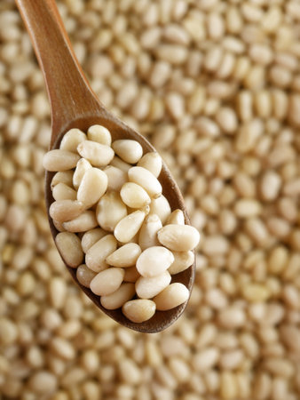 Cleaned pine nuts. Pine nut kernels lie in wooden spoon. Top view of nuts close-up. Advertising photography for marketplaces or online stores.の写真素材