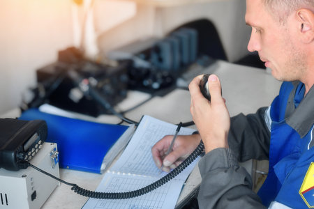 Man of Caucasian appearance receives signal on walkie-talkie and writes message in journal. Receiving distress call or important message via radio. Dispatcher sends coordinates.の写真素材