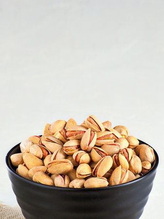 Pistachios in shell are poured into cup. Frontal front view with copy space. Preparation of layout for sale of pistachios in online store or marketplaces. Vertical photo.の写真素材