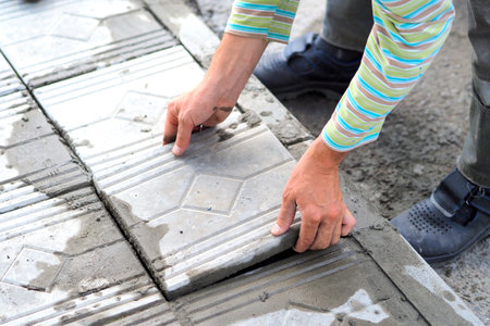 Worker tiler lays tiles with cement outside on summer day. Authentic workflow. Hands with facing tiles.の写真素材