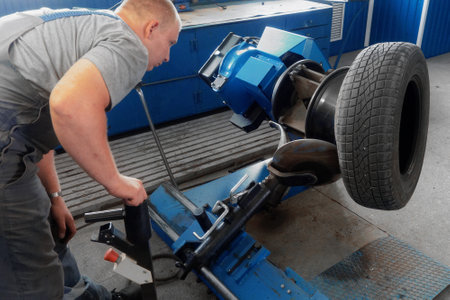 Car mechanic works in tire shop. Mechanic removes wheel from disk with special device. Replacing wheel tire in garage. Professional service.の写真素材