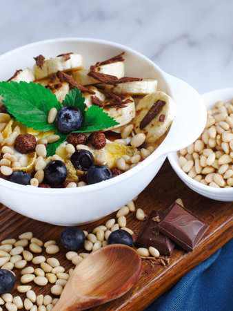 Useful breakfast. Fruit salad with banana, pine nuts, blueberries, chocolate and corn flakes. Fitness recipe for healthy balanced breakfast. Still life. Top view.の写真素材