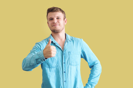 Handsome young caucasian man in denim shirt showing thumbs up on yellow background. Positive confident man. Approving gesture. Looks into camera.の写真素材