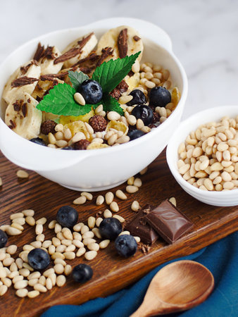 Useful breakfast. Fruit salad with banana, pine nuts, blueberries, chocolate and corn flakes. Fitness recipe for healthy balanced breakfast. Still life. Top view.の写真素材