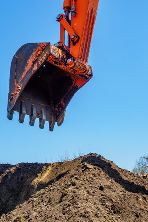 Excavator digs hole in ground. View of excavator bucket against blue sky on pile of earth. Construction site. Background.の写真素材