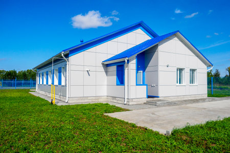 New one-story house. Front side of house is on green lawn against blue sky. Construction of industrial facilities. Background.の写真素材