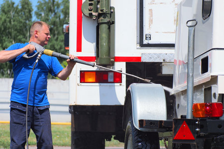 Car wash for heavy and cargo vehicles. Male car washer in washes a truck with a water gun on the street on a summer day.の写真素材