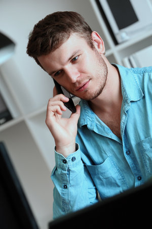 A young handsome man is talking on a mobile phone. A Caucasian guy is sitting in a room and talking on the phone. Vertical portrait.の写真素材