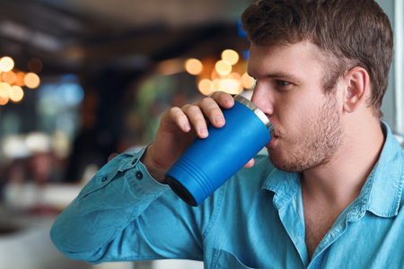 Man drinks drink or coffee from flask mug. Side view Mockup with copy space. Young Caucasian guy...
