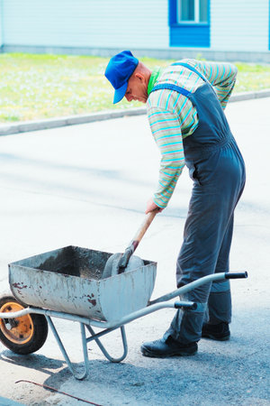 Male builder mixes cement mortar with shovel outside on summer day. Worker works at construction site. Builder prepares cement.の写真素材