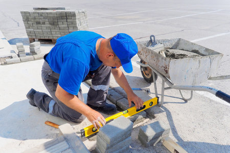 Professional bricklayer works at construction site and lays brick foundation. Man in uniform is working on porch on summer day. Authentic workflow.の写真素材