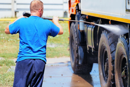 Car wash for heavy and cargo vehicles. Male car washer in washes a truck with a water gun on the street on a summer day.の写真素材