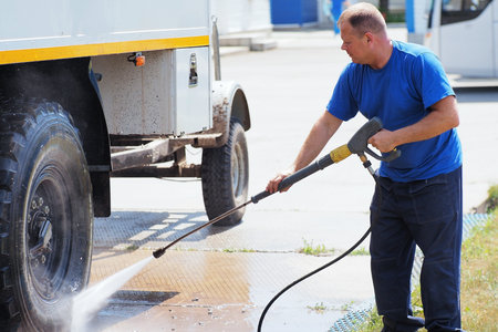 Car wash for heavy and cargo vehicles. Male car washer in washes a truck with a water gun on the street on a summer day.の写真素材