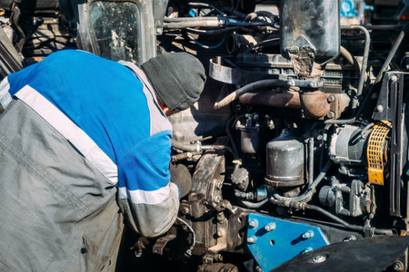 Working mechanic repairs tractor with keys. Close-up view from back. Man repairs equipment.の写真素材