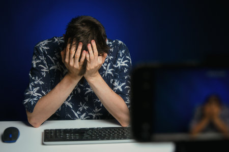 Tired and disappointed guy sitting in front of a phone camera at a home studio table, depressed....