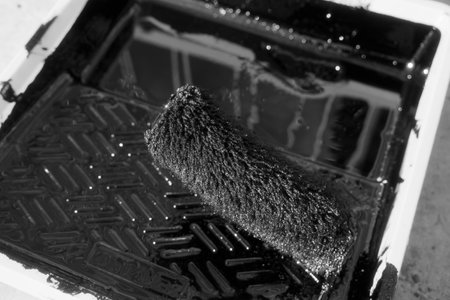 Paint roller in tray with black industrial paint or primer. Top view of paint roller with paint tray. Industrial background.の写真素材