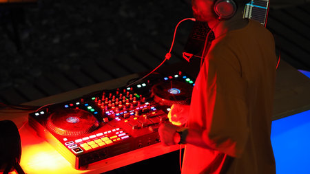 DJ wearing headphones stands at music console in nightclub.の写真素材