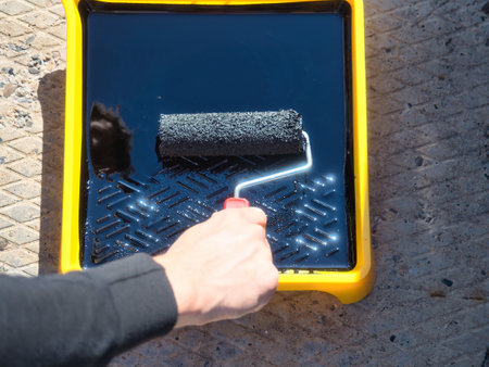 Industrial repair and painting. Painters hand with paint roller over tray of black paint. Background.の写真素材