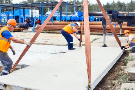 Professional builders work on construction site. Team of slingers lay concrete slab on ground on summer day. Real workflow.の写真素材