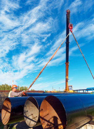 New pipes for gasification. Worker in construction helmet ships large-diameter metal pipes. Industrial background with copy space.の写真素材