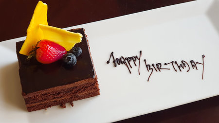Birthday dessert. Piece of cake with strawberries lies on plate. Happy birthday inscription with chocolate.の写真素材