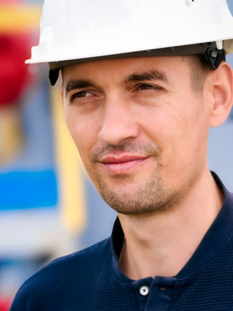 Portrait of Caucasian builder or gas industry engineer wearing white construction helmet. Confident looking working man aged 35-40 stands against background of yellow pipes. Reliable contractor.の写真素材