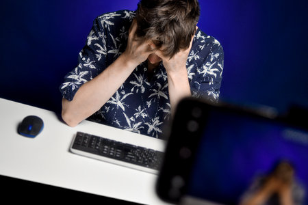 Tired and disappointed guy sitting in front of a phone camera at a home studio table, depressed. Crisis of ideas. Professional blogger burnout.の写真素材