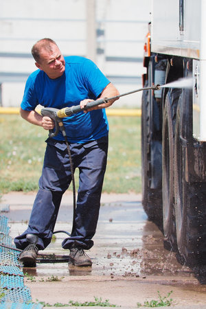 Car wash for heavy and cargo vehicles. Male car washer in washes a truck with a water gun on the street on a summer day.の写真素材