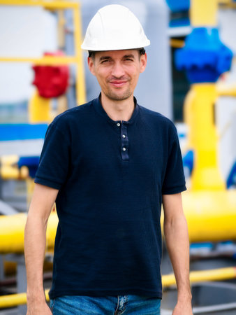 Portrait of Caucasian builder or gas industry engineer wearing white construction helmet. Confident looking working man aged 35-40 stands against background of yellow pipes. Reliable contractor.の写真素材