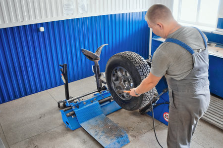 Car mechanic inflates car wheel with compressor in tire repair shop. Mechanic changes tires on wheel, balances and inflates tire. Professional car service.の写真素材
