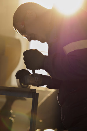 Metal mechanic works with angle grinder in factory workshop. Backlit cinematic light. Photo. Portrait of real man at work. Grinds metal.の写真素材
