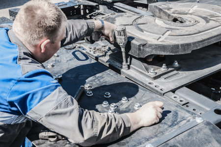 A man is working on a piece of machinery. He is wearing a blue shirt and gray pants