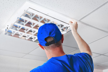 A professional is fixing a fluorescent light grille panel in the suspended ceiling of an office building. Wearing a blue cap and shirt, the persons ensure proper alignment and safety.の写真素材