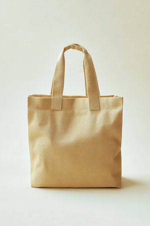 A beige tote bag stands upright on a soft light background, emphasizing its minimalistic design and sturdy fabric. This versatile bag is ideal for everyday use, shopping, or casual outings, making it a practical choice.の素材
