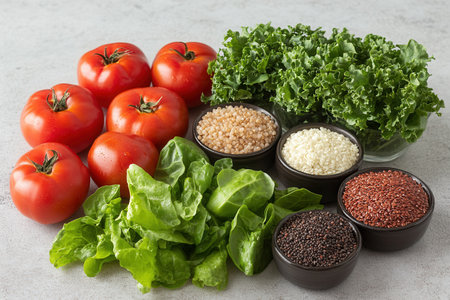 A vibrant collection of fresh tomatoes, leafy greens, and assorted grains is beautifully arranged on a gray surface. This composition showcases the colorful ingredients perfect for healthy meal preparation and cooking.の素材