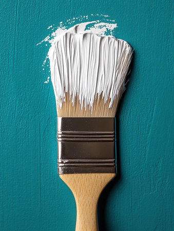 A paintbrush coated with white paint rests against a turquoise wall, showcasing a fresh application of color. This moment captures the essence of a home renovation, highlighting creativity and transformation.の素材