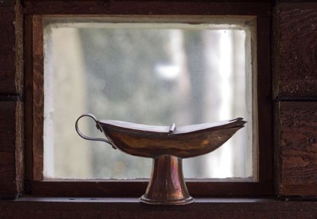antique cupper oil lamp in front of small barn window in wooden wallの写真素材