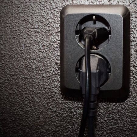 Black socket with two black plugs in dark wall