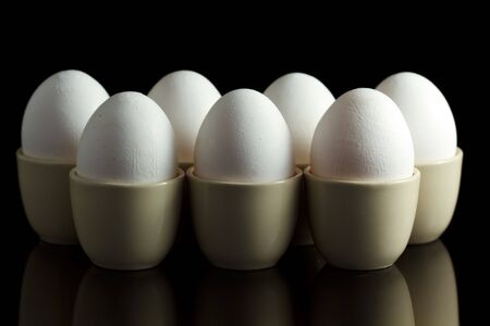 white chicken eggs in egg-cups on black reflecting backgroundの写真素材