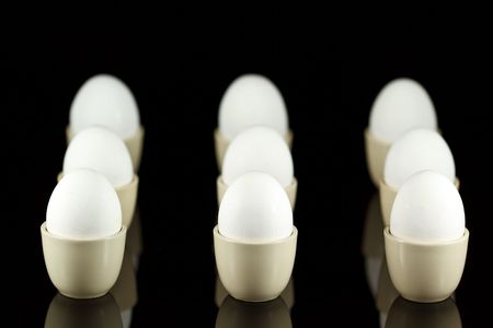 white chicken eggs in egg-cups on black reflecting backgroundの写真素材