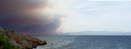 Forrest fire in Spain makes a dramatic sky over a bay at the costa bravaの写真素材