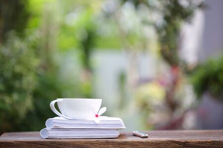 White coffee cup and notebooks on wooden table at outdoor