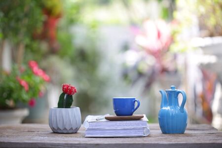 Blue cup with small cactus plant and diary notebook with blue jar on wooden table at outdoor
