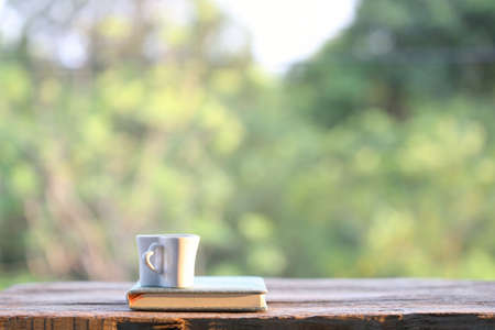 White cup with notebook on wooden table with nature viewの写真素材