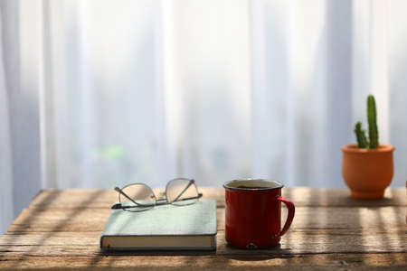 Red coffee cup and glasses with green notebook and cactus pot on rustic wooden tableの写真素材