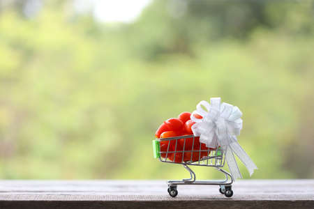 Small Tomatoes in mini shopping basket with white ribbon on wooden tableの写真素材