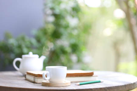 White tea kettle and white cup with notebook and pencil on wooden table outdoor viewの写真素材