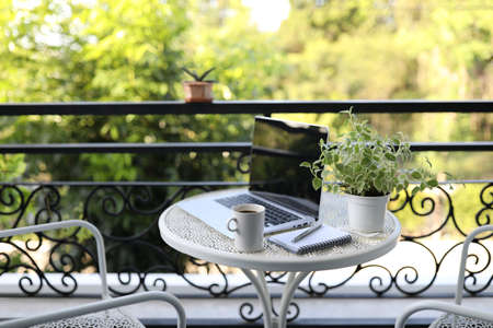Laptop with coffee cup and plant pot on metal table at corridor